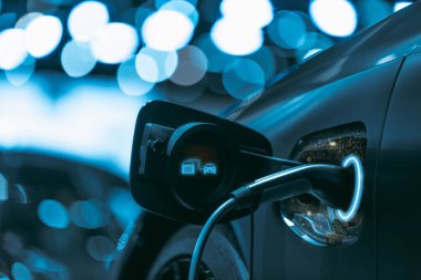 Bir istasyonda şarj edilen elektrikli bir aracın yakın çekim görüntüsü, modern mavi ışıklar fütüristik ve yenilikçi bir hava yaratıyor..