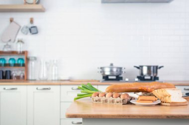 Yumurta, ekmek, sosis ve yeşil soğan da dahil olmak üzere ahşap tezgahta taze malzemelerle dolu parlak, modern bir mutfak.. 