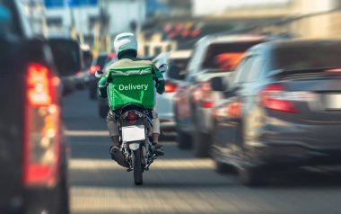 Ağır şehir trafiğinde zikzak çizen motosikletli teslimat şoförü, hızlı servisi ve modern lojistik zorlukları simgeliyor.