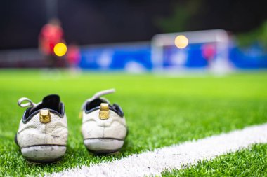 Futbol kramponları gece antrenmanı sırasında kale direğinin yanında ısınan bulanık oyuncular gibi yapay sahada dinleniyor..