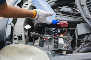 Eldiven takan biri araç bakımında araba aküsüne damıtılmış su döker. Otomotiv aküsü bakımının kaput altı görüntüsü.