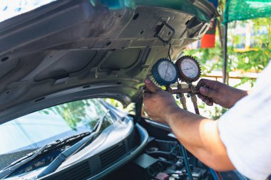 Kaput altındaki araba havalandırma sistemini kontrol etmek ve hizmet etmek için manifold göstergesi kullanan tamirci.