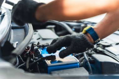 Kaputun altına akü yerleştirirken ya da yerleştirirken eldiven takan tamirci ellerinin yakın çekimi.