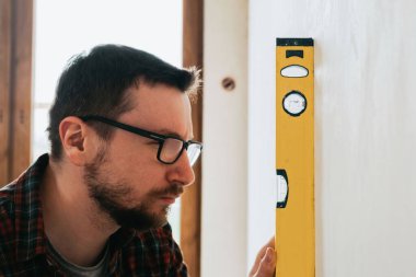 İnşaat alanındaki inşaatçı, ruhsal seviyeye odaklanarak tesisat ölçüyor.