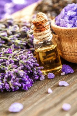 Ahşap bir masanın üzerinde kurutulmuş lavanta çiçekleri olan lavanta spa ürünleri. Tahta zemine banyo tuzu ve masaj yağı serpiştirilmiş. Cilt bakımı, güzellik tedavi konsepti. Lavendula oleum