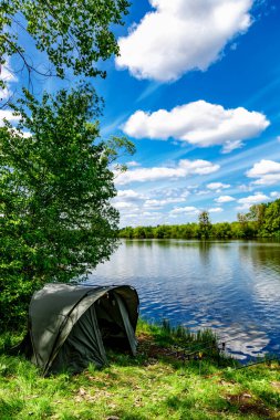 Carpfishing session at the Lake.Carp Angling scenic landscape overlooking lake at and blue sky with clouds.Fishing adventures, carp fishing. clipart