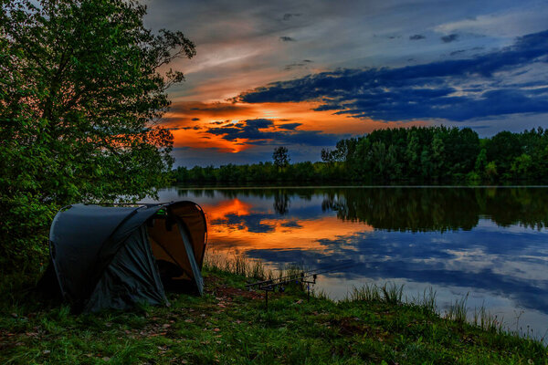 Fishing adventures, carp fishing. Angler, at sunset, is fishing with carpfishing technique. Camping on the shore of the lake.Carp Fishing Sunset