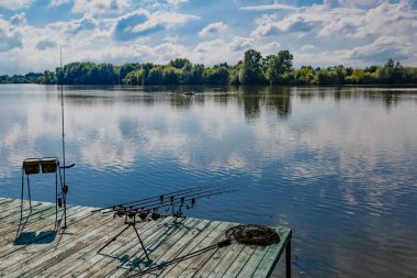 Gölde balık avı. Özel tripodların üzerinde sazan balığı avlama çubukları. Sazan balığı, göle bakan manzaralı ve bulutlu mavi gökyüzü..