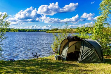 Gölde balık avı. Sazan balığı, göle bakan manzaralı bir manzara ve bulutlu mavi gökyüzü. Gölün kıyısında kamp..