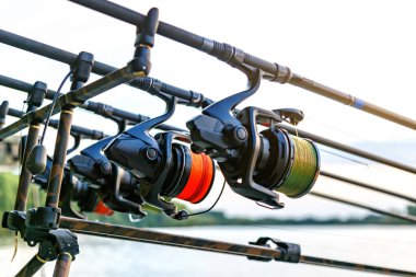 Gölde balık avı. Sazan oltaları özel tripodların üzerinde duruyor. Şafak vakti göle bakan manzaralar..