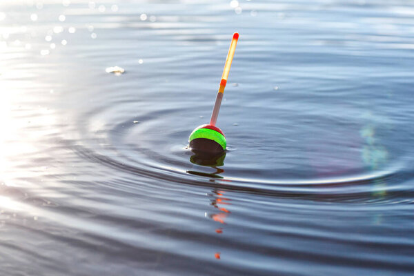 Fishing float on the water surface with circles around.Fishing adventures, carp fishing.Catching of fish.The blue sky is reflected in the water. Fish are biting