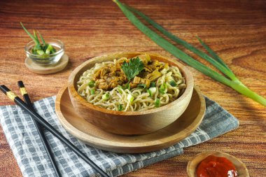 Tavuklu erişte, Endonezya 'da Mie Ayam olarak bilinir. Ahşap arka planda bir kasede yeşil sebze sosuyla servis ediliyor. Üst görünümü kapat düz görünüm alanı oluştur