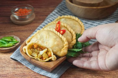 Pastel Goreng olarak bilinen Endonezya 'daki kızarmış pasteller. Elle ahşap bir tabakta çiğ biberle servis edilen sebze, tavuk ve haşlanmış yumurtayla dolu kızarmış hamur işi. Kapat.