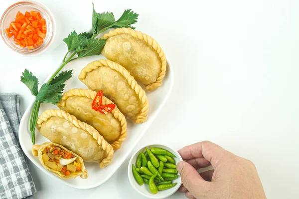 stock image Fried pastels, in Indonesia known as Pastel goreng. Fried pastry with filling of vegetable , chicken and boiled egg served with raw chilli in a plate on white background with hand. Top view copy space