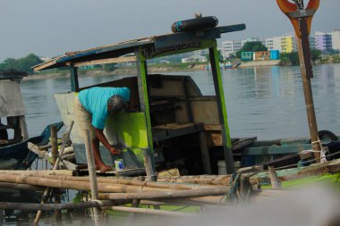 Bir balıkçı teknesini Jakarta 'da bir nehrin kıyısına boyuyor.