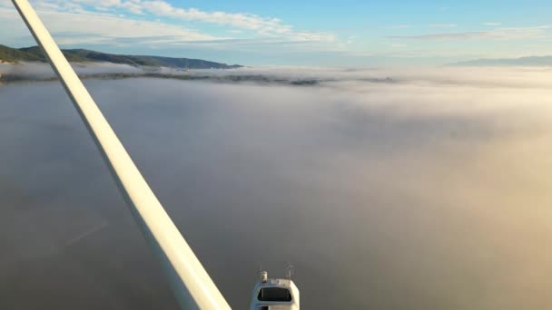 日の出高密度の朝の霧の間にドローンのショット風力タービン クローズアップ風力タービン クリーングリーンエネルギーを生産する風車 — ストック動画