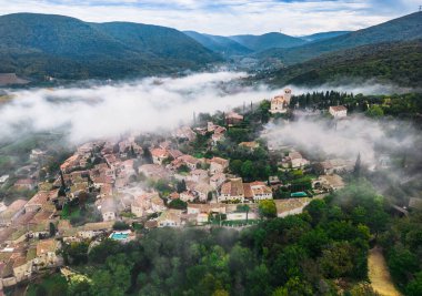 Fransa 'nın Mirmande köyünün panoramik manzarası. Sabahleyin şehrin etrafında yükselen yoğun siste havadan çekilmiş bir fotoğraf.