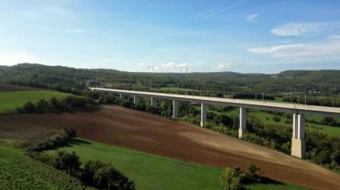 Dağlardaki tünele akan yüksek üstgeçitteki yüksek hızlı trenlerin panoramik görüntüsü. Arka planda yeşil enerji üreten bir rüzgar çiftliği var. Bir İHA 'dan Uçuş