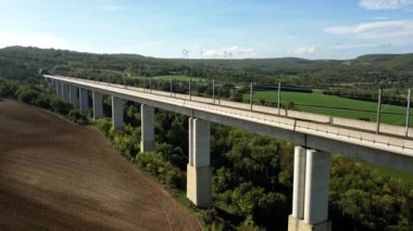 Dağlardaki tünele akan yüksek üstgeçitteki yüksek hızlı trenlerin panoramik görüntüsü. Arka planda yeşil enerji üreten bir rüzgar çiftliği var. Bir İHA 'dan Uçuş