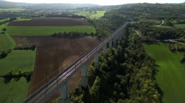 Dağlardaki tünele akan yüksek üstgeçitteki yüksek hızlı trenlerin panoramik görüntüsü. Arka planda yeşil enerji üreten bir rüzgar çiftliği var. Bir İHA 'dan Uçuş