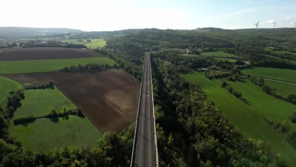 全景全景铁路轨道高速列车在高架桥上流入隧道的山脉 在后台是一个风力发电场 产生绿色能源 从无人机上逃跑 — 图库视频影像