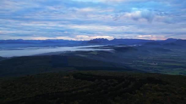 谷に閉じ込められた朝の霧が山の反対側に流れます 朝のフランスアルプスのパノラマビュー 遠くの濃霧の中の風力発電所 — ストック動画