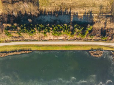 Sunset over a frozen lake. Sunbeams falling on water. Shadows of trees on the ice covering the lake. Aerial view of a frozen lake. Ice sheet background. Frozen grass in water