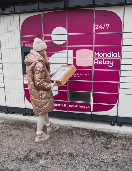 Loriol sur Drome, France - January 14, 2023: Picking up a parcel from a Mondial `Relay locker by a young woman. Lockers Mondial Relay. Pickup box a place by the road to send and receive parcels.