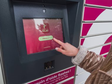 Loriol sur Drome, France - January 14, 2023: Picking up a parcel from a Mondial `Relay locker by a young woman. Lockers Mondial Relay. Pickup box a place by the road to send and receive parcels.