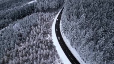Panoramic winter view from above over the forest. Cinematic winter snowy rural asphalt road with cars driving through snowy forest. Forests covered with snow. Cinematic winter frosty landscape.
