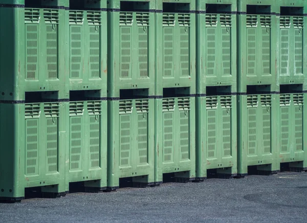 Big green plastic crates for fruits are stacked and waiting to be filled with fruits, apples, pears. Big industrial fruit crates stored outside, stacked in piles.