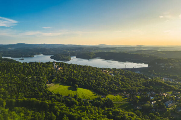 Panoramic view from the drone during sunset, on Lake Solina overlooking the modern gondola lift with a lookout tower over the Solina water dam, in the Polish Bieszczady Mountains, Poland
