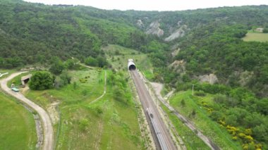Yüksek hızlı bir yolcu treninin dağın eteğinden tünele girerken panoramik drone görüntüsü. Güney Fransa 'daki dağlara tepeden bakan