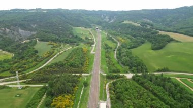 Yüksek hızlı bir yolcu treninin dağın eteklerindeki tünelden çıkarken panoramik drone görüntüsü. Güney Fransa 'daki dağlara tepeden bakan