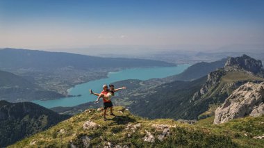Annecy Gölü ve Fransız Alpleri 'ne tepeden bakan uçurumun kenarında duran genç çift, panoramik yaz dağı ve göl manzarası