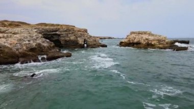 Bulgaristan 'daki mavi, yeşil, turkuaz dalgaların, manzaralı deniz kayalıklarına ve keskin kayalara çarptığı havadan insansız hava aracı görüntüleri. Yüksek kalite 4k görüntü