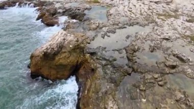 Bulgaristan 'daki mavi, yeşil, turkuaz dalgaların, manzaralı deniz kayalıklarına ve keskin kayalara çarptığı havadan insansız hava aracı görüntüleri. Yüksek kalite 4k görüntü