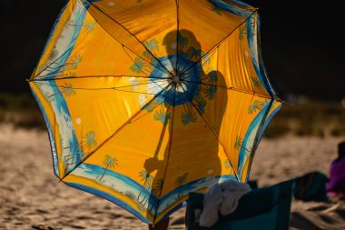 Plaj yaz şemsiyesinin arkasındaki bir kişinin silueti. Plaj deniz konsepti. Renkli sarı yaz gölge şemsiyesi. Yüksek kalite fotoğraf