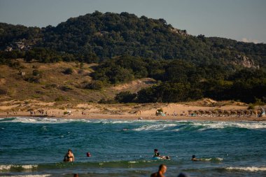 August 11, 2023: Sozpol, Bulgaria - The beautiful beach coast Arkutino in Sozpol municipality. People swimming in the water. Hills and forest in the distant background. High quality photo clipart