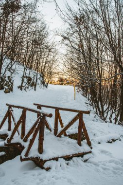 Bulgaristan 'ın Vitosha dağ parkındaki tahta köprü. Köprü karla kaplı. Kış zamanı. Güzel beyaz kar. Ağaçların arkasında gün batımı.