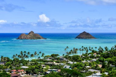 Açık mavi okyanus suyu ve iki küçük ada. Avuçlar plaj tarafında ve evler. Beyaz bulutlu mavi gökyüzü. Oahu, Hawaii 'nin güzel manzarası. Yüksek kalite fotoğraf. Yüksek kalite fotoğraf