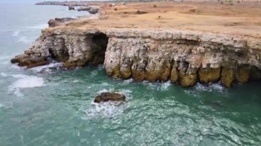 Bulgaristan 'daki mavi, yeşil, turkuaz dalgaların, manzaralı deniz kayalıklarına ve keskin kayalara çarptığı havadan insansız hava aracı görüntüleri. Yüksek kalite 4k görüntü