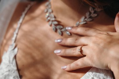 Gelinliği içinde güzel bir gelin kolyesine dokunuyor. Perde camından ışık geliyor. Yüksek kalite fotoğraf