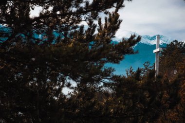 Architecture observation lookout point structure in Razlog, Bulgaria. White cross statue in Autumn winter time shot through tree branches. Snowy mountain Pirin. clipart