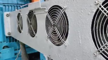 Metal bir panele monte edilmiş dört endüstriyel soğutma vantilatörünün yakın çekimi. Taraftarlar dairesel ve siyah metal ızgaraları var. Panel beyaza boyanmış ve yıpranmış görünüyor..