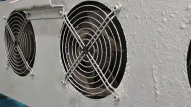 Metal bir panele endüstriyel soğutma vantilatörü monte edildi. Taraftarlar dairesel ve siyah metal ızgaraları var. Panel beyaza boyanmış ve yıpranmış görünüyor.