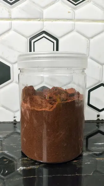 stock image a glass jar of coffee in a transparent cup. the concept for a coffee break. A clear plastic jar with a white lid contains a full amount of coffee powder, sitting on a black countertop with a white hexagonal tile backsplash.