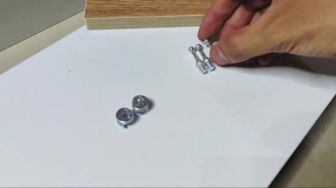 Adamın eli, beyaz bir tahta üzerine minyatür cıvatalar ve vidalar yerleştirir..