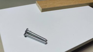 Bir adamın eli beyaz tahta hareketinin üstüne iki tane düz vida yerleştirir ve bir tane daha düz vida ekler. Reklam endüstrisi ve imalat için klip