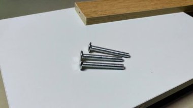 Bir adamın eli beyaz tahta hareketinin üstüne iki tane düz vida yerleştirir ve bir tane daha düz vida ekler. Reklam endüstrisi ve imalat için klip